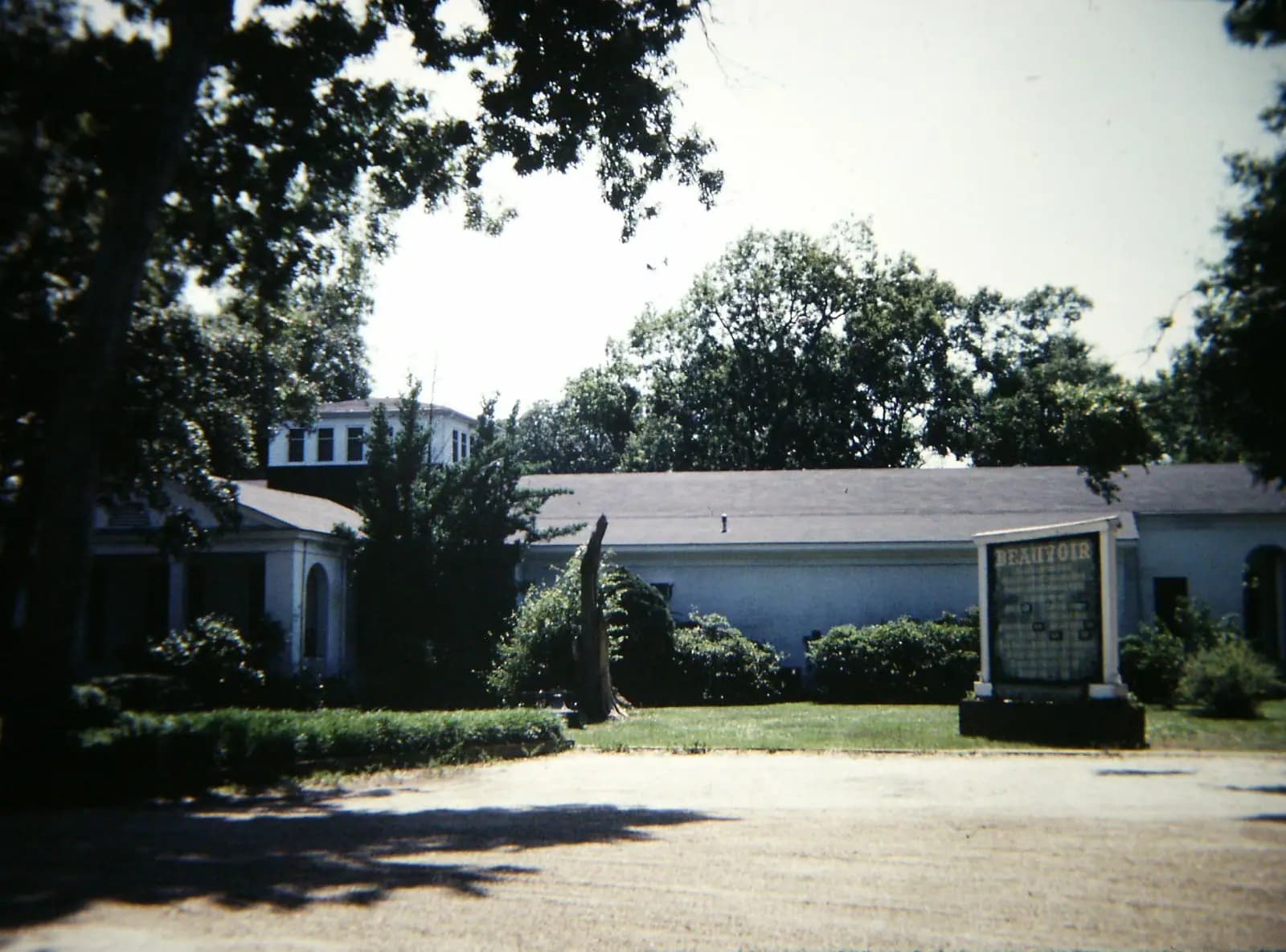 A wooden house with wide verandahs shaded by mature trees