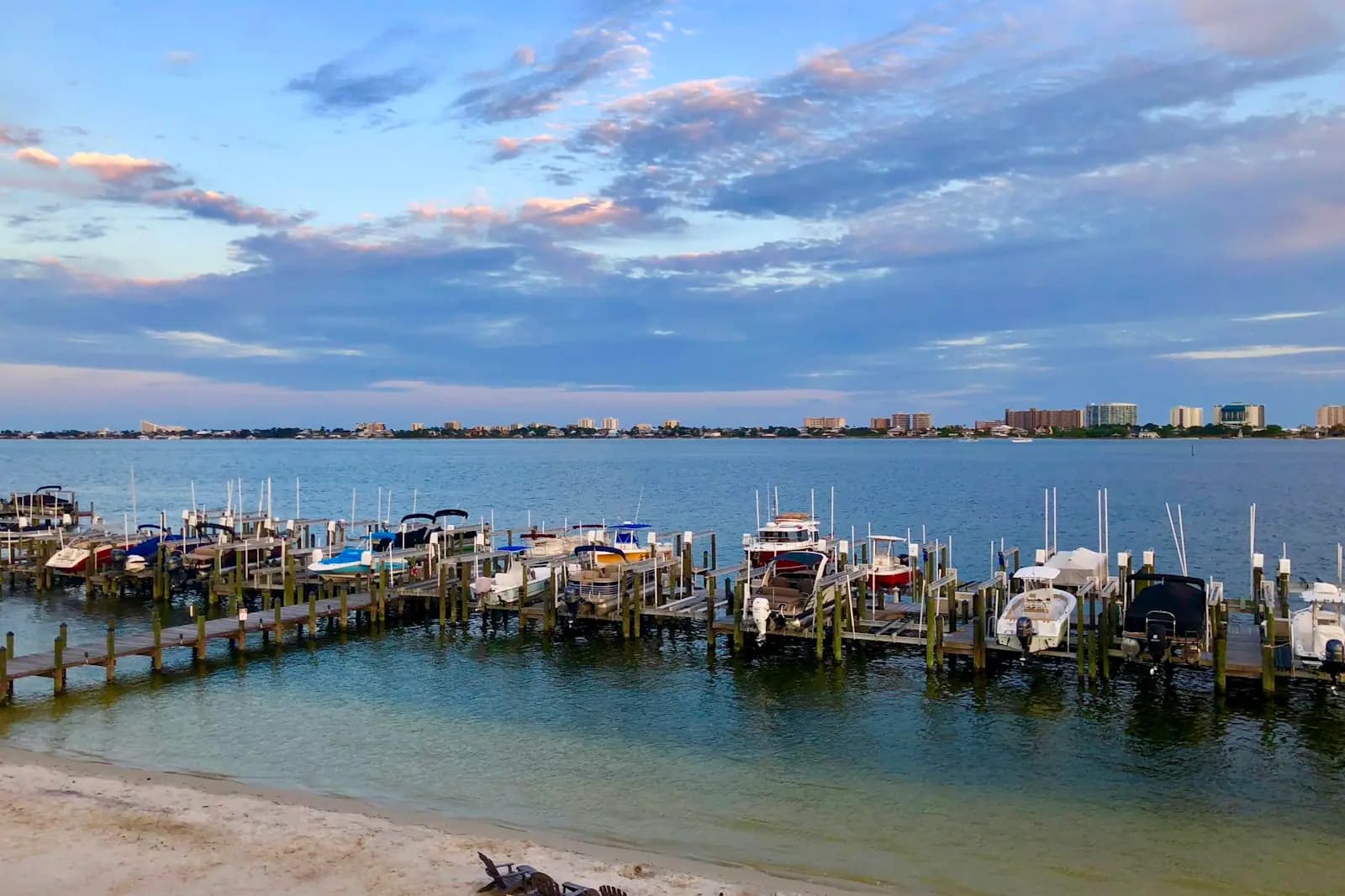 Small boats moored along finger docks in a shallow bay basin with a low shoreline beyond at dusk