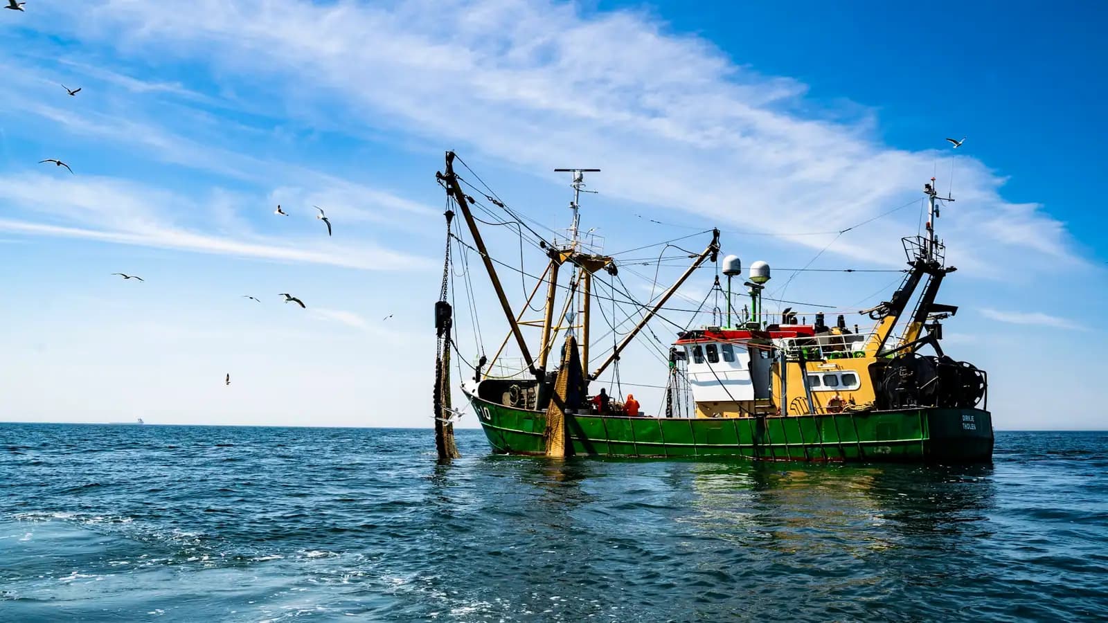 A working trawler under way on open water with its outrigger booms rigged out and gulls following astern