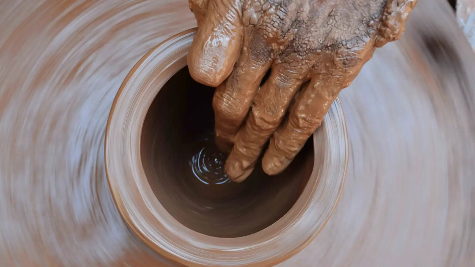 A potter's hands shaping wet clay on a spinning wheel