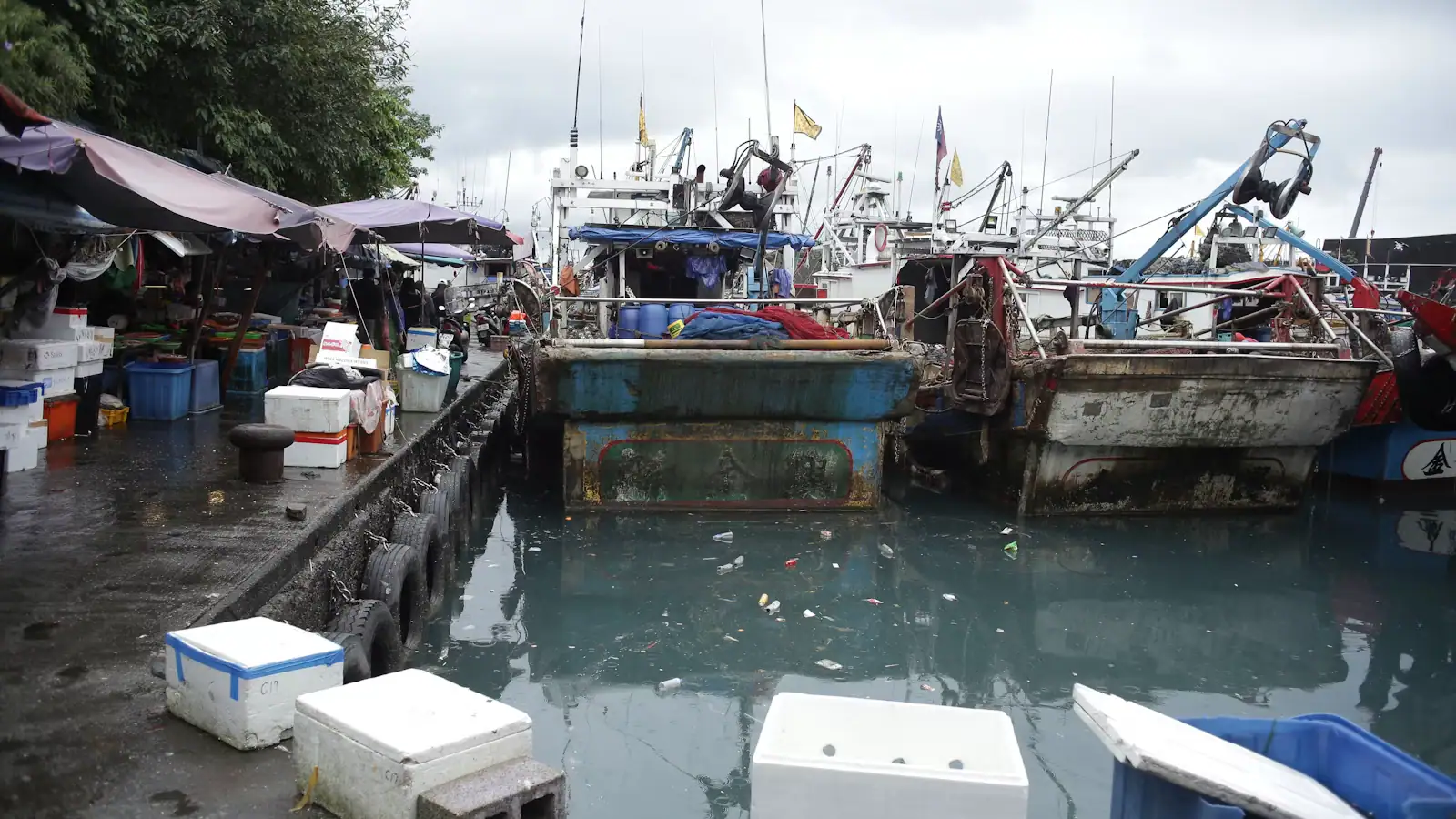 Working fishing boats tied along a harbour dock under a low overcast sky
