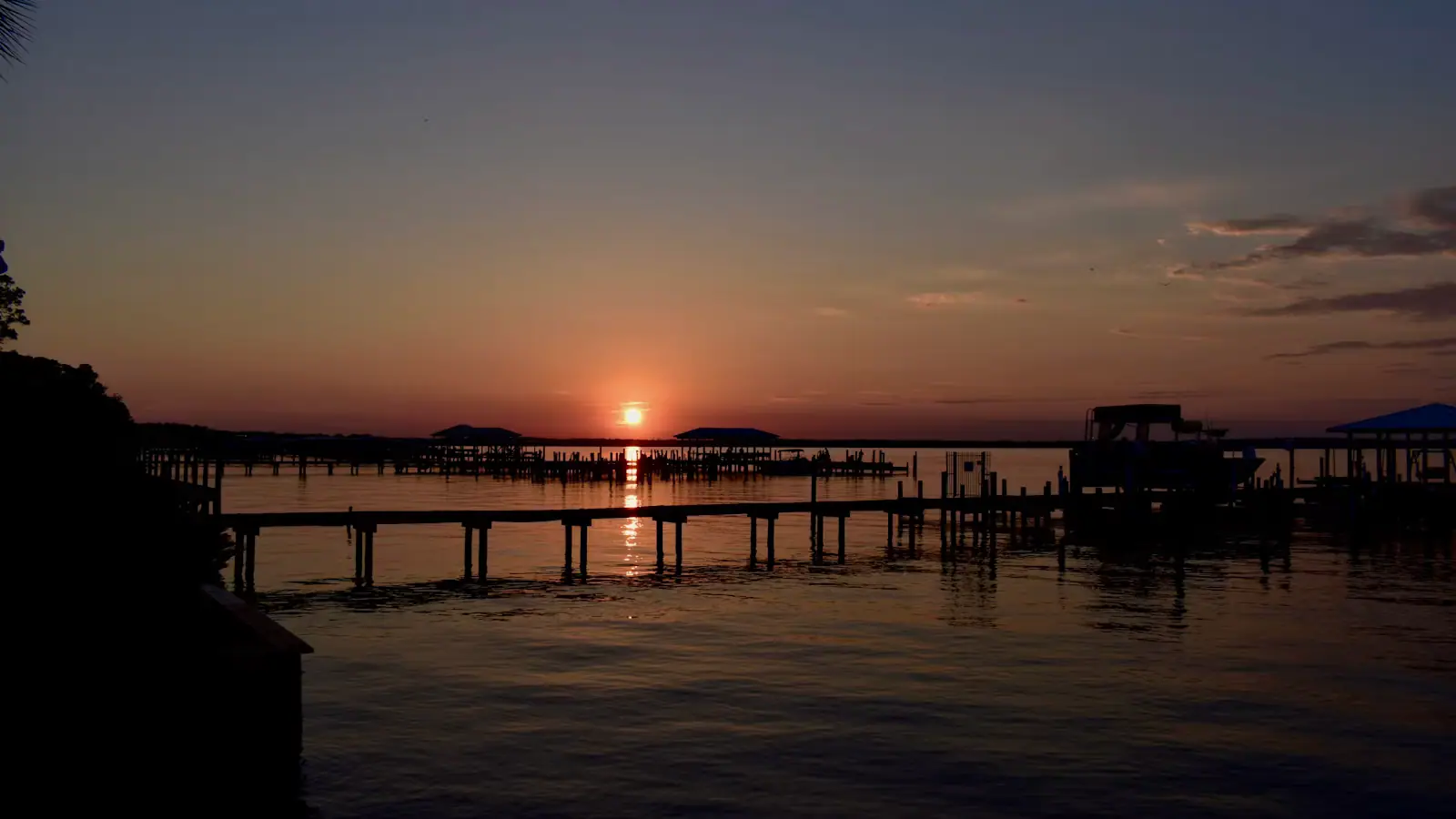 A silhouetted dock reaching out over calm water at sunset
